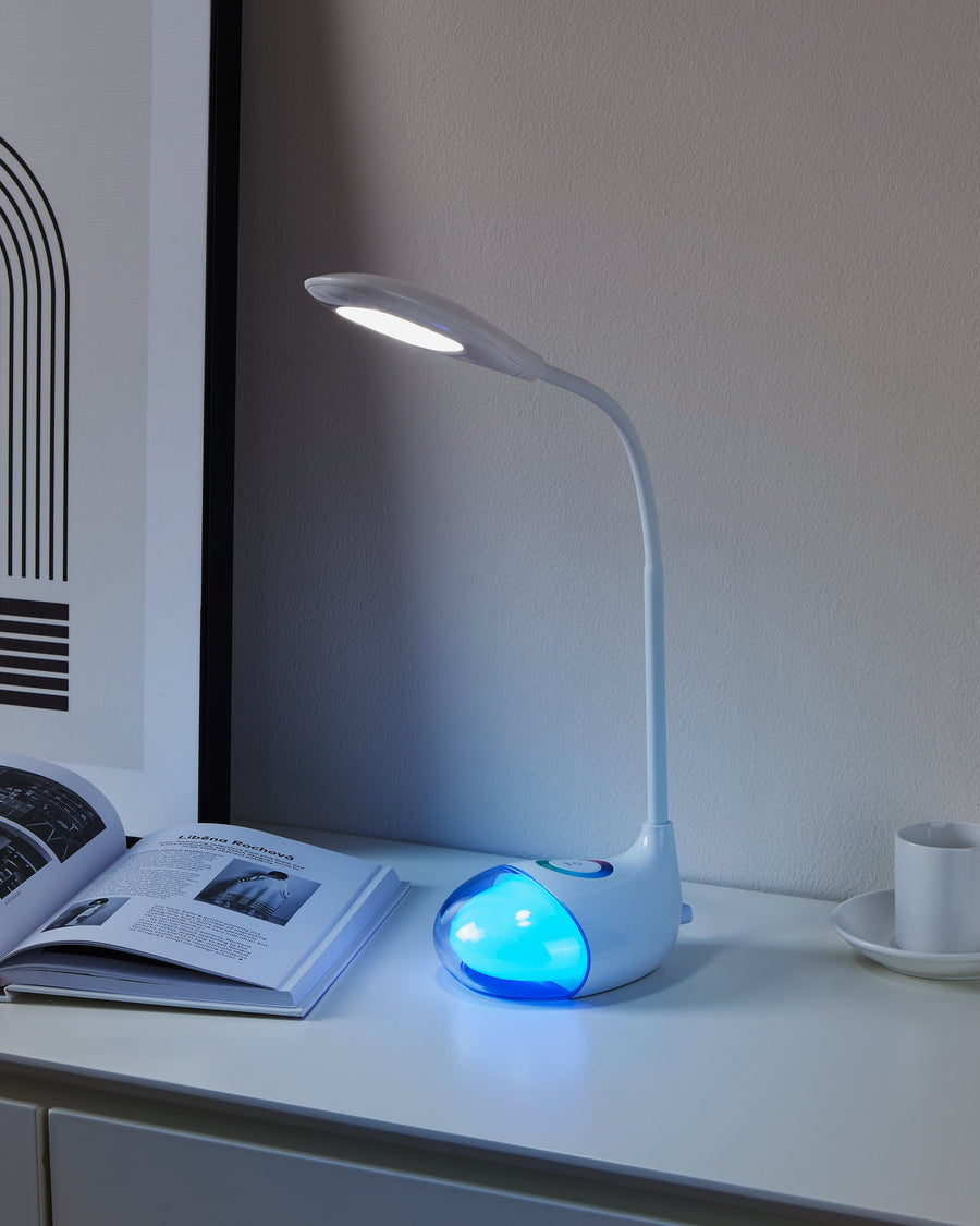 Lampe allumée sur meuble blanc, lumière bleue près d'un livre et d'une tasse.