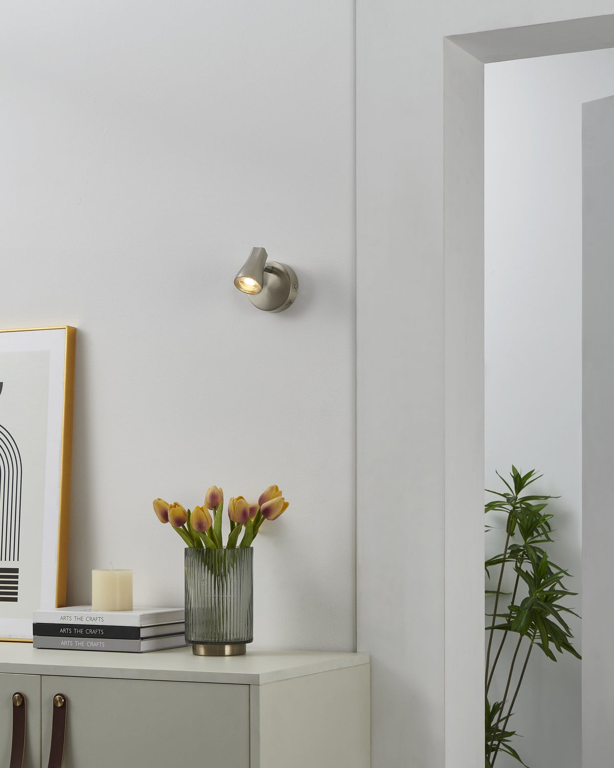 Mise en ambiance : spot allumé sur mur blanc, cadre, tulipes et plante verte