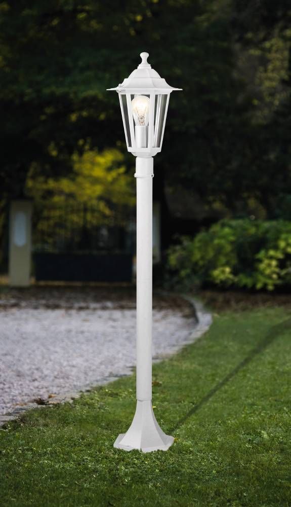 Lampadaire blanc installé dans un jardin, lanterne allumée, mise en ambiance extérieure.