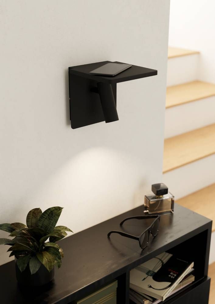 Applique murale noire avec tablette supportant un smartphone, éclairant un mur blanc.