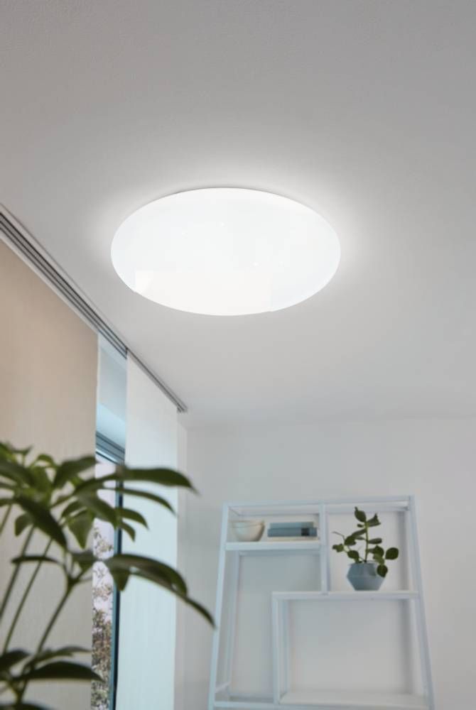 Plafonnier blanc allumé au plafond dans un salon avec étagère et plantes.