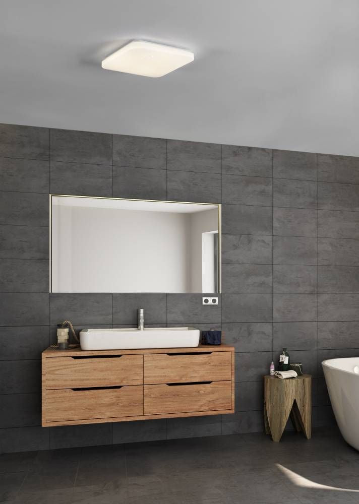 Plafonnier éclairé dans une salle de bain en carrelage gris avec meuble en bois