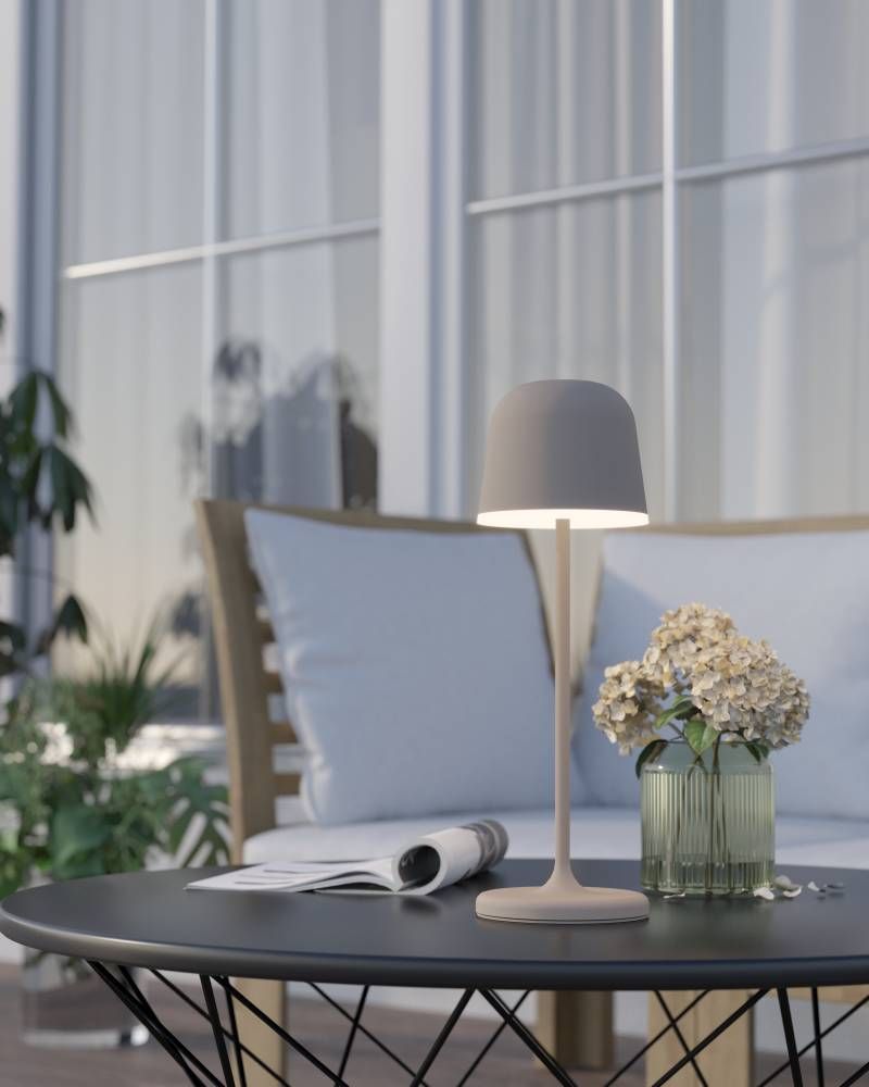 Lampe allumée posée sur une table basse, entourée d'un magazine et d'un vase de fleurs.