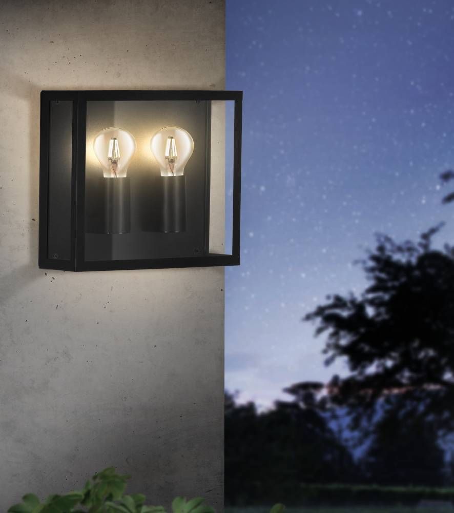Applique extérieure noire allumée sur un mur, ciel étoilé et silhouette d'arbre la nuit.