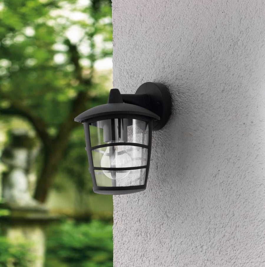 Luminaire mural noir fixé sur un mur crépité, feuillage vert flou en arrière-plan