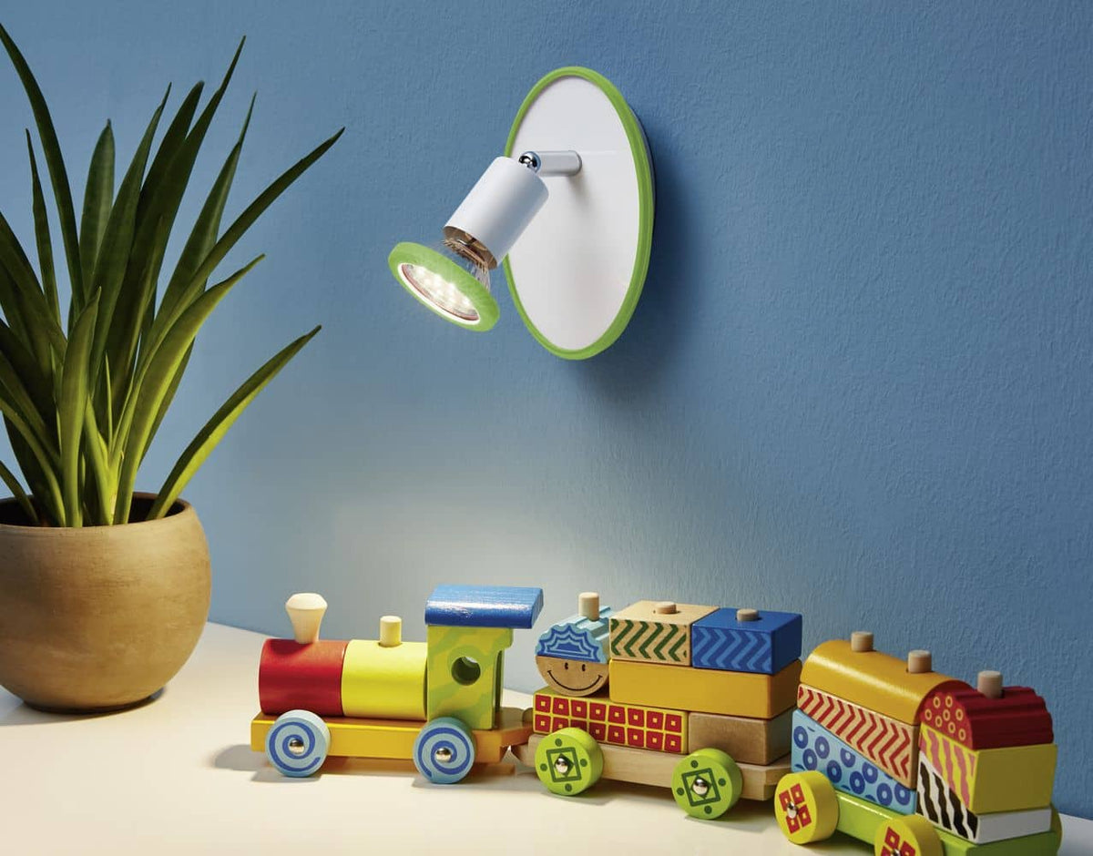 Mise en ambiance dans une chambre d'enfant, spot mural vert orienté vers des jouets en bois