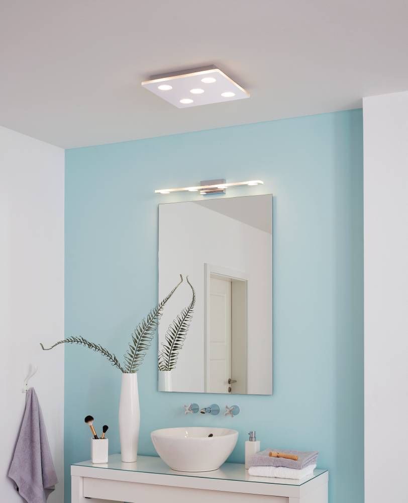 Applique murale chromée allumée au-dessus d'un miroir dans une salle de bain bleue.