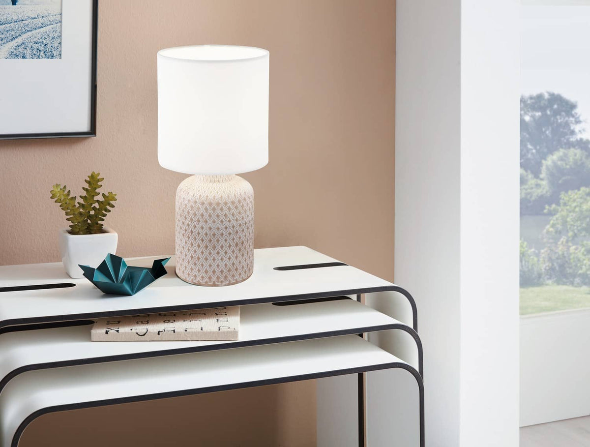 Lampe allumée sur une table basse blanche, près d'une plante et d'une grue en papier