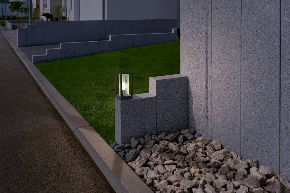 Mise en ambiance nocturne du luminaire posé sur un muret en pierre près d'une pelouse