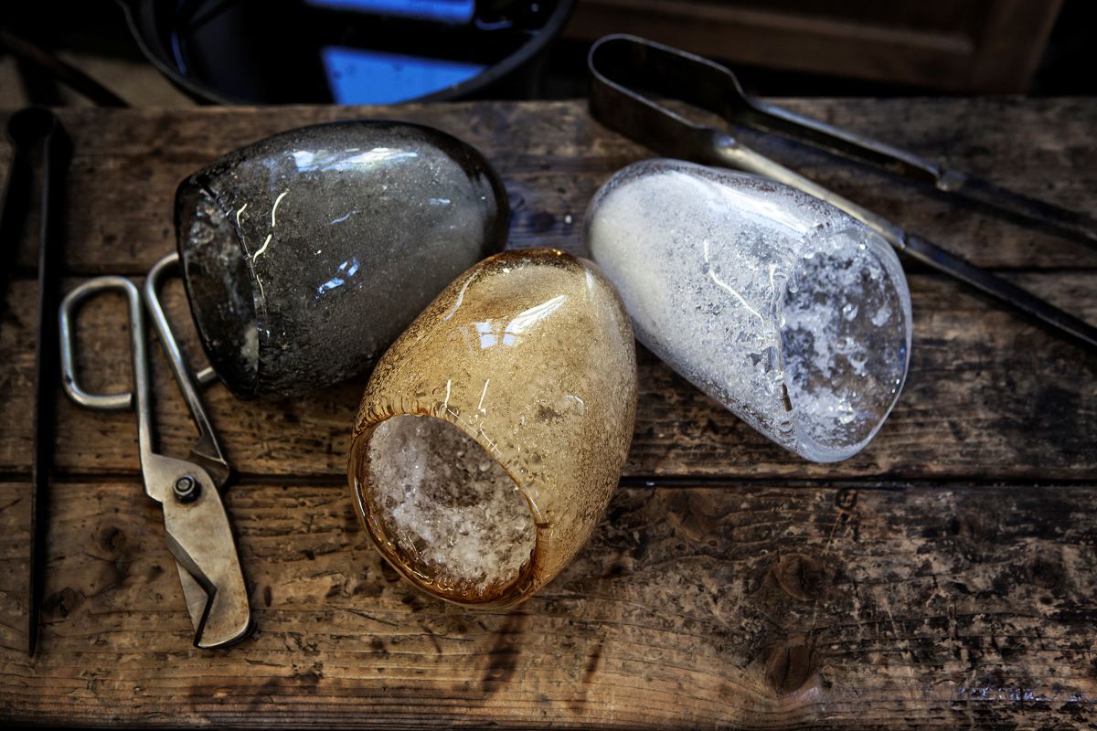 Atelier de soufflage montrant les abat-jour en verre brut et les outils du verrier.