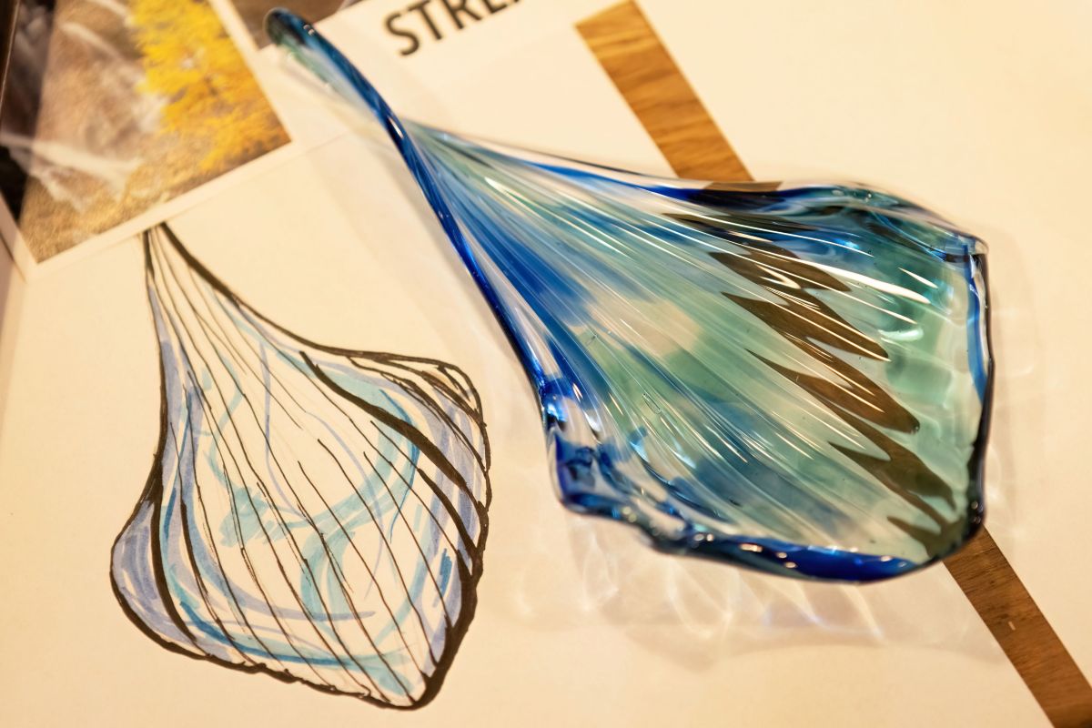 Gros plan sur une goutte de verre bleu soufflé posée sur un croquis dessiné.