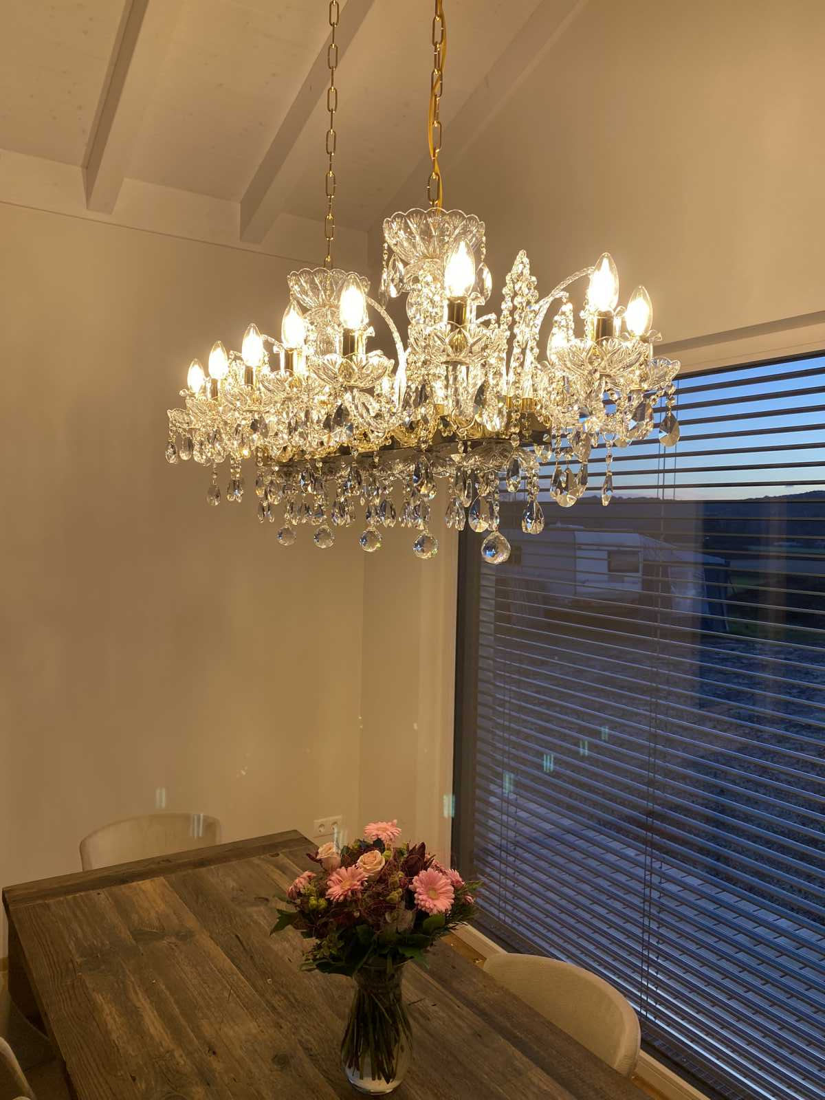 Vue rapprochée du lustre illuminé, gouttes de cristal et ampoules au-dessus de la table.