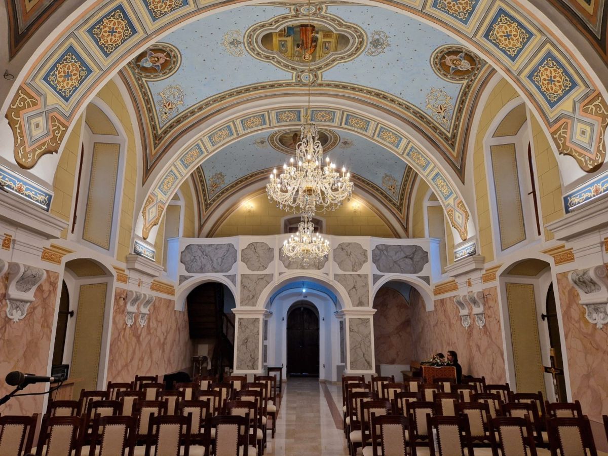 Lustre allumé au centre d'une église ornée, vu depuis le fond de la salle.