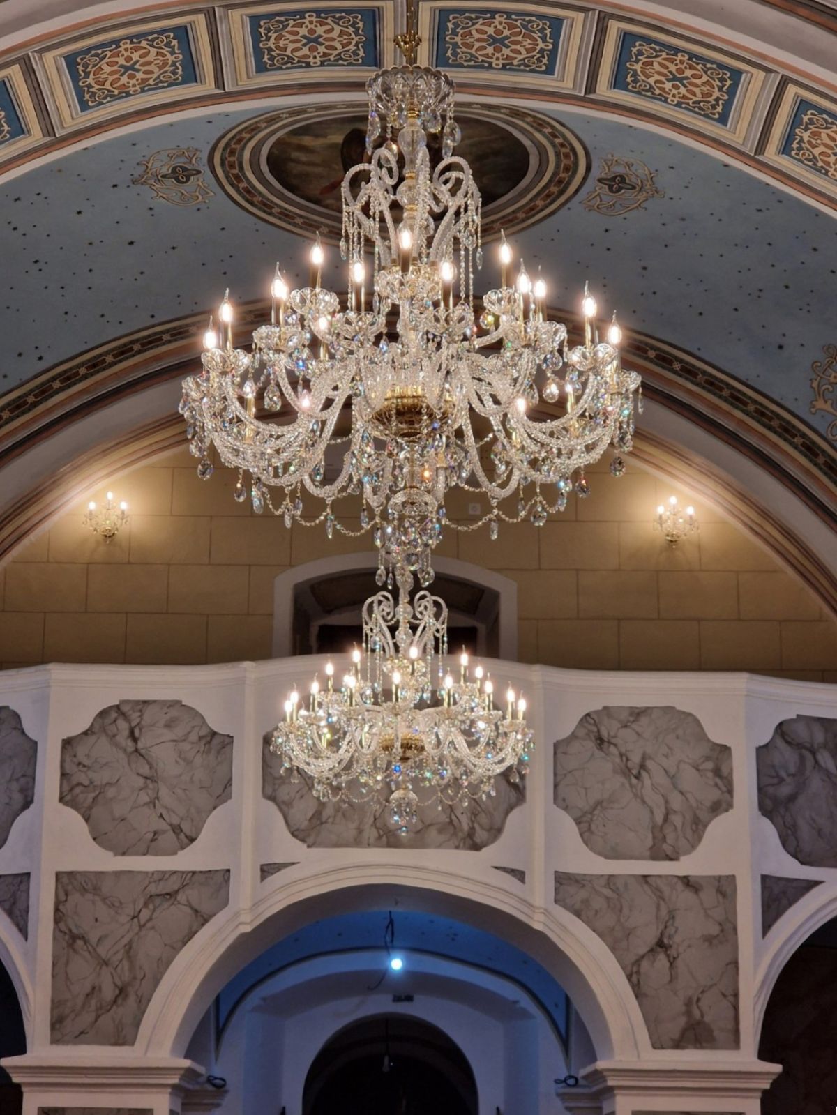 Vue en contre-plongée du lustre sous une voûte décorée, éclairé dans une église.