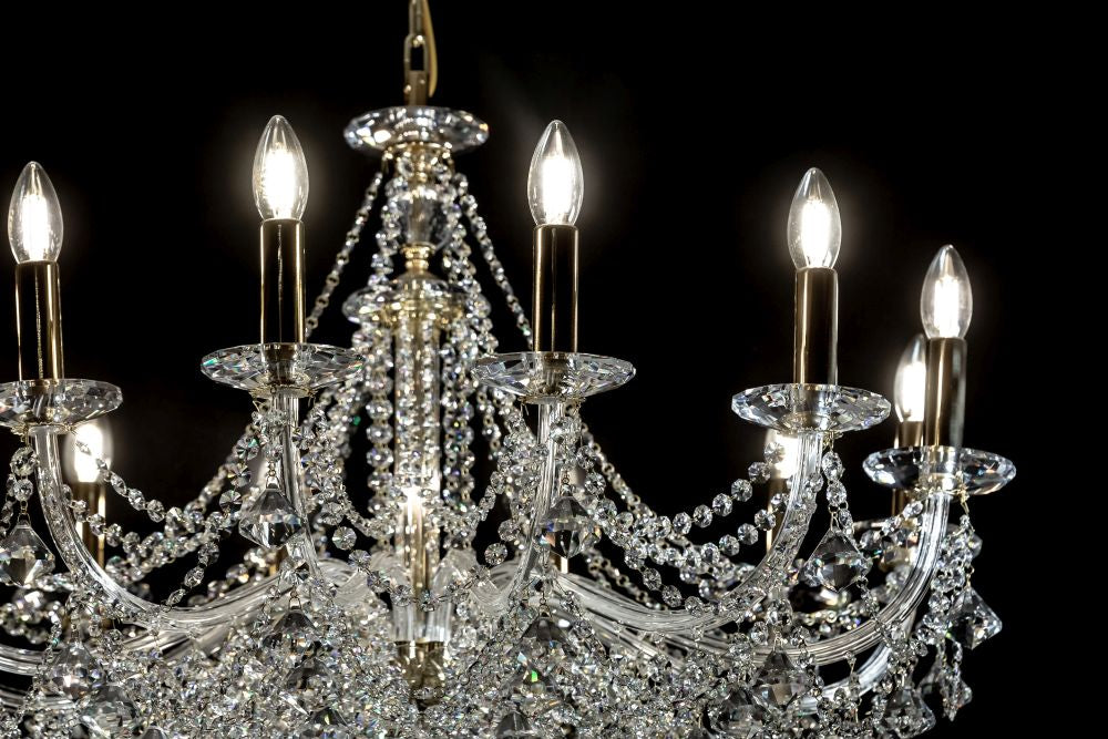 Gros plan sur les ampoules allumées du lustre, éclairant les bras et les chaînes de cristal.