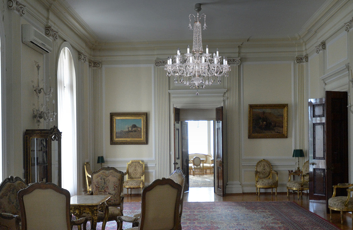 Mise en ambiance du lustre suspendu au centre d'un salon classique aux dorures anciennes.