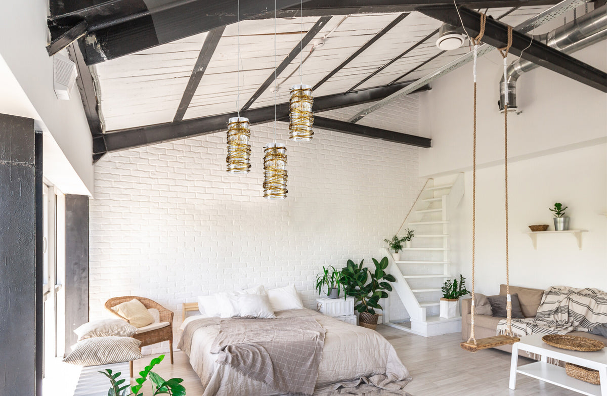 Trois suspensions en verre ambré éclairant un loft blanc avec lit, poutres noires et plantes vertes.