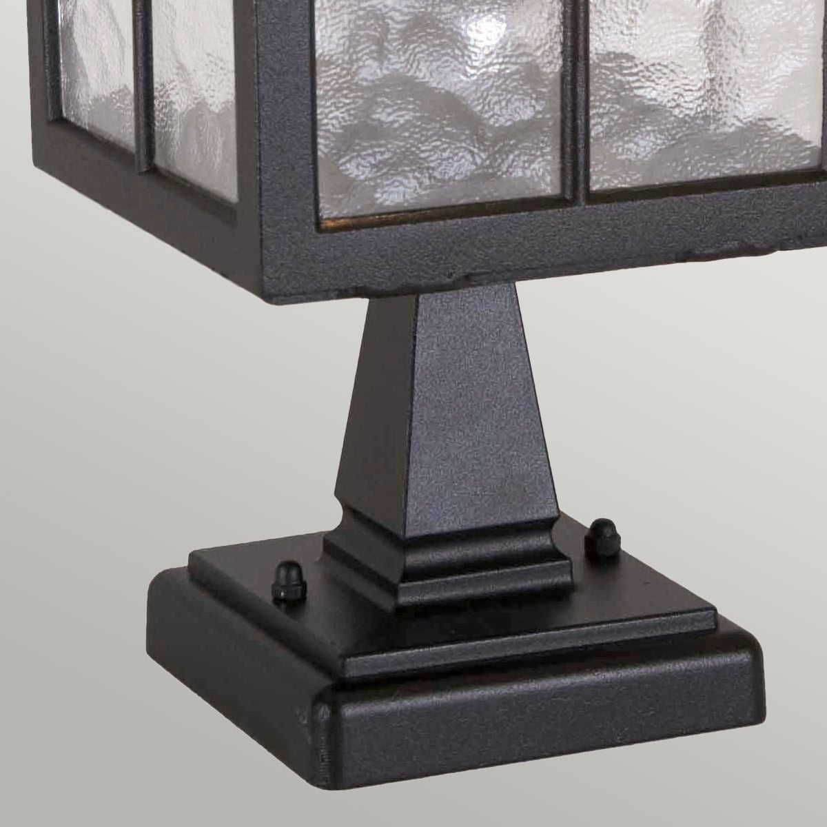 Détail de la base carrée noire avec vis de fixation et socle mouluré.