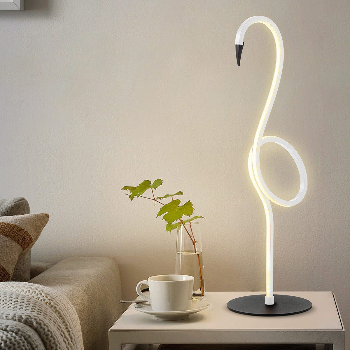 Lampe flamant blanche allumée posée sur une table de chevet avec tasse