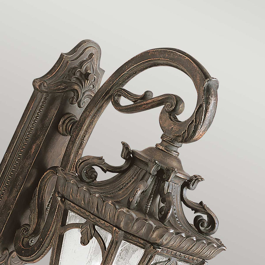 Détail du bras recourbé et des volutes ornées, finition bronze vieilli de l'applique.