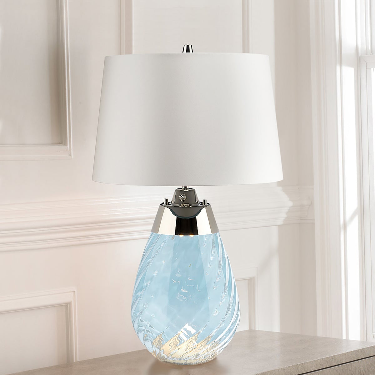 Lampe allumée posée sur un meuble devant un mur blanc