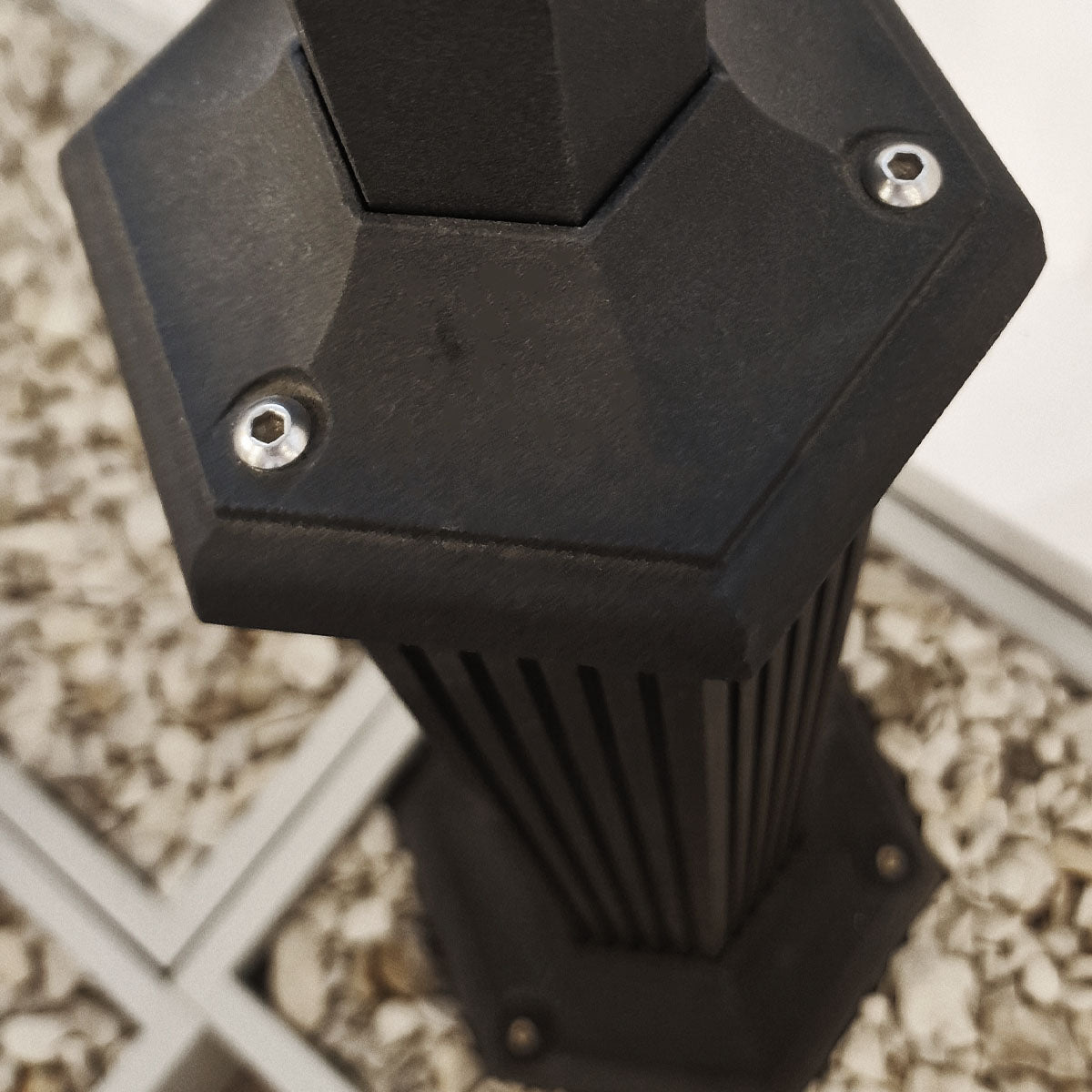 Détail du socle hexagonal noir et de ses vis de fixation en métal argenté.
