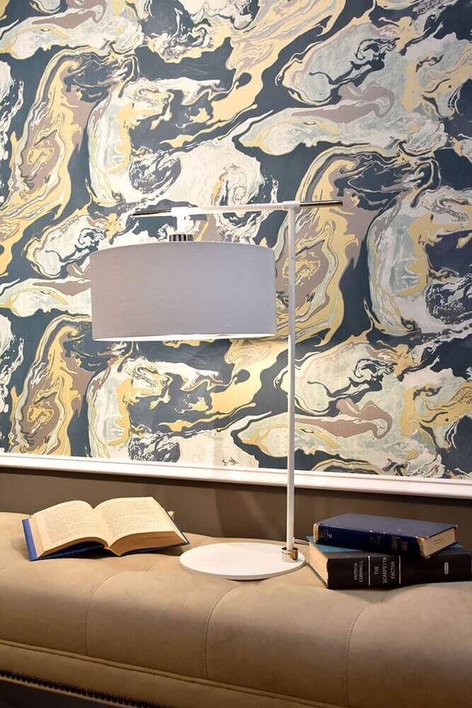 Lampe posée sur un banc taupe devant un papier peint marbré bleu et doré