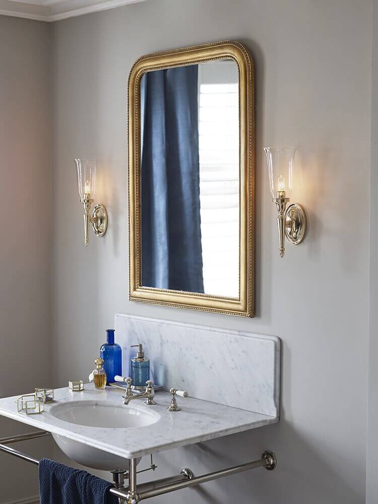 Applique murale installée de chaque côté d'un miroir doré au-dessus d'un lavabo en marbre.