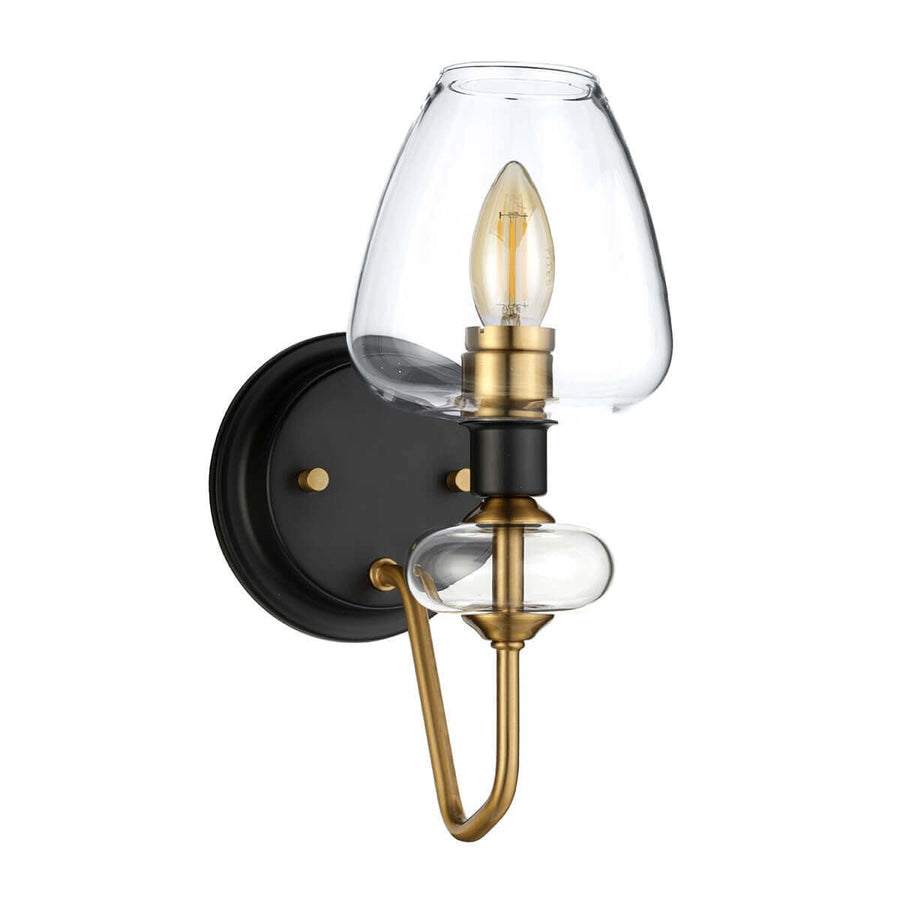 Détail de l'abat-jour en verre transparent et du bras en laiton sur support noir.