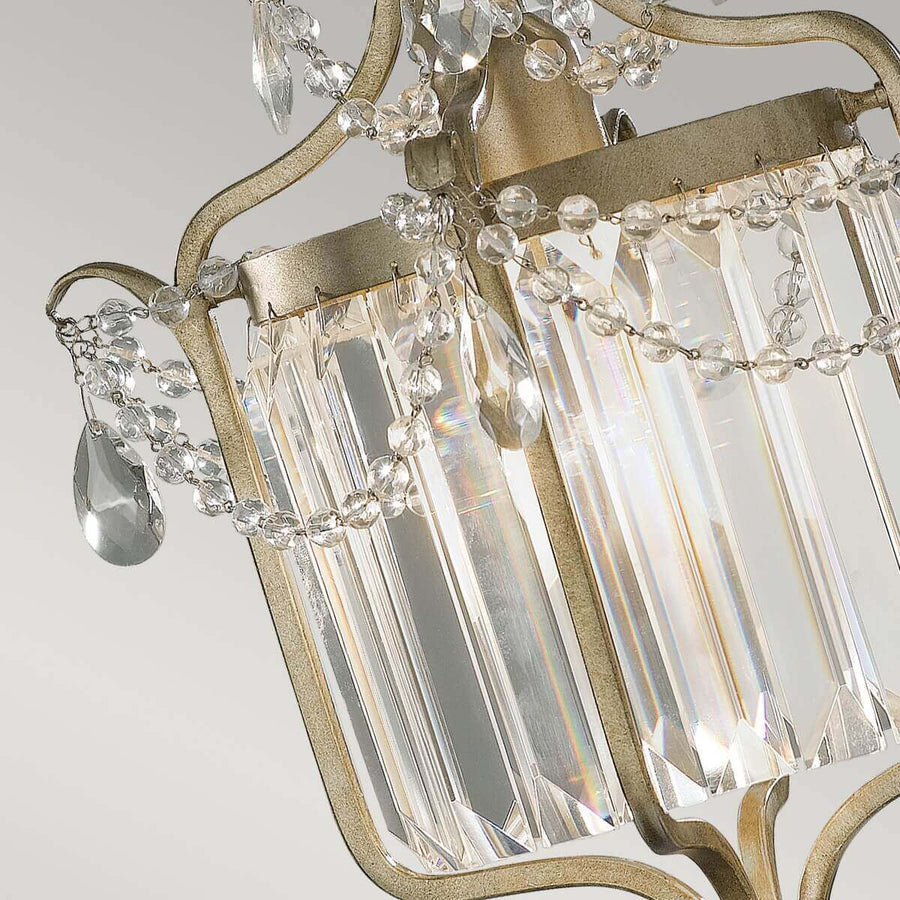 Gros plan sur les prismes de cristal, chaînette perlée et reflets irisés sur la structure métallique.