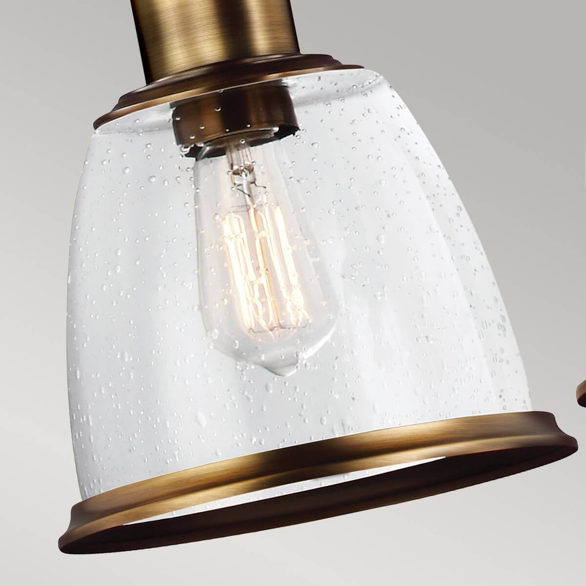Détail d'un abat-jour en verre clair moucheté avec ampoule Edison allumée à l'intérieur.