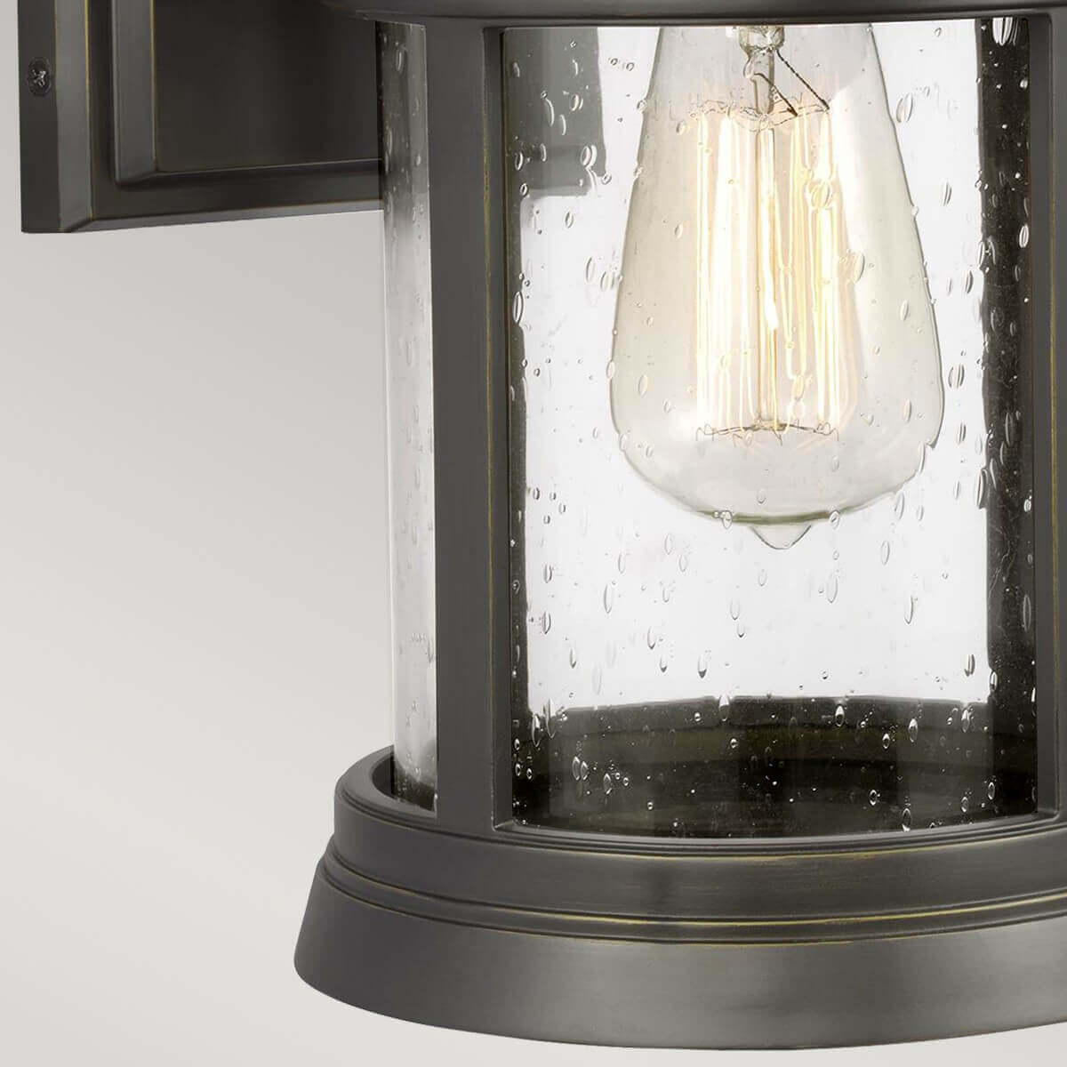 Détail du bas, ampoule à filament allumée derrière le verre perlé et la base moulurée
