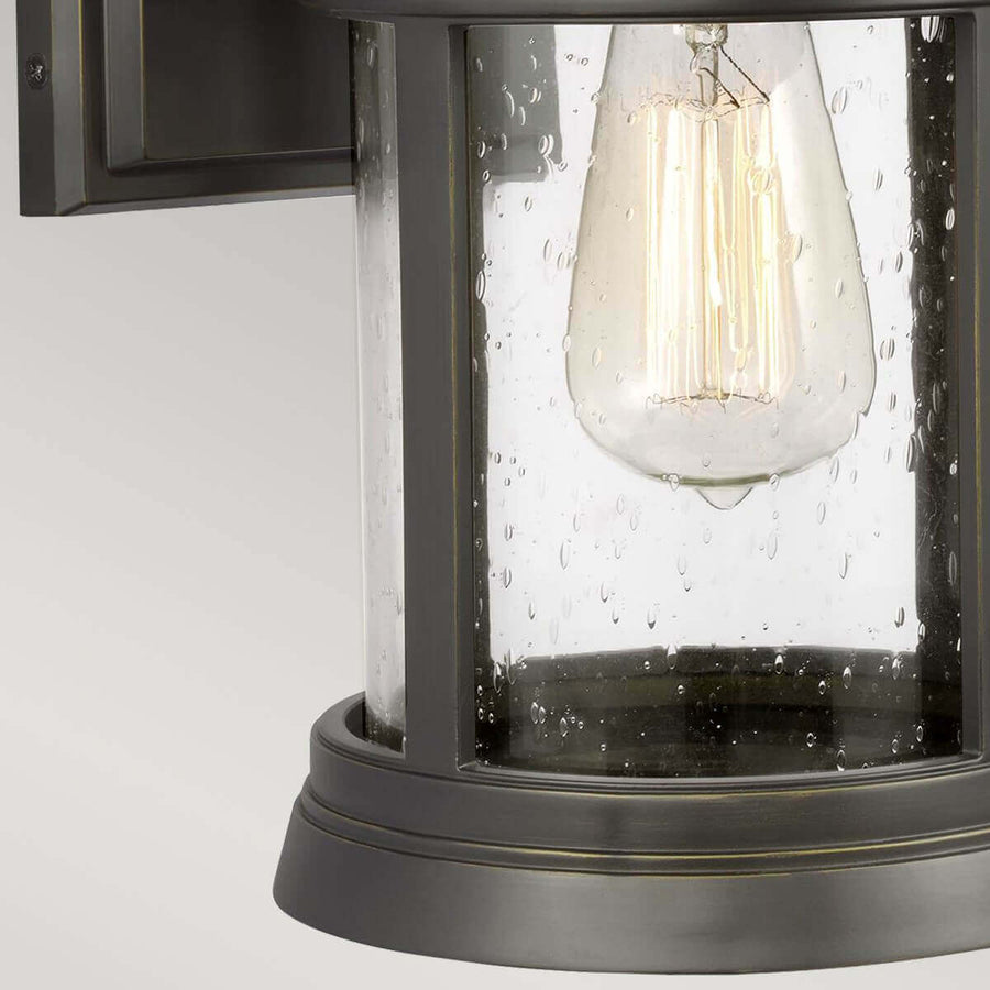 Détail du bas, ampoule à filament allumée derrière le verre perlé et la base moulurée