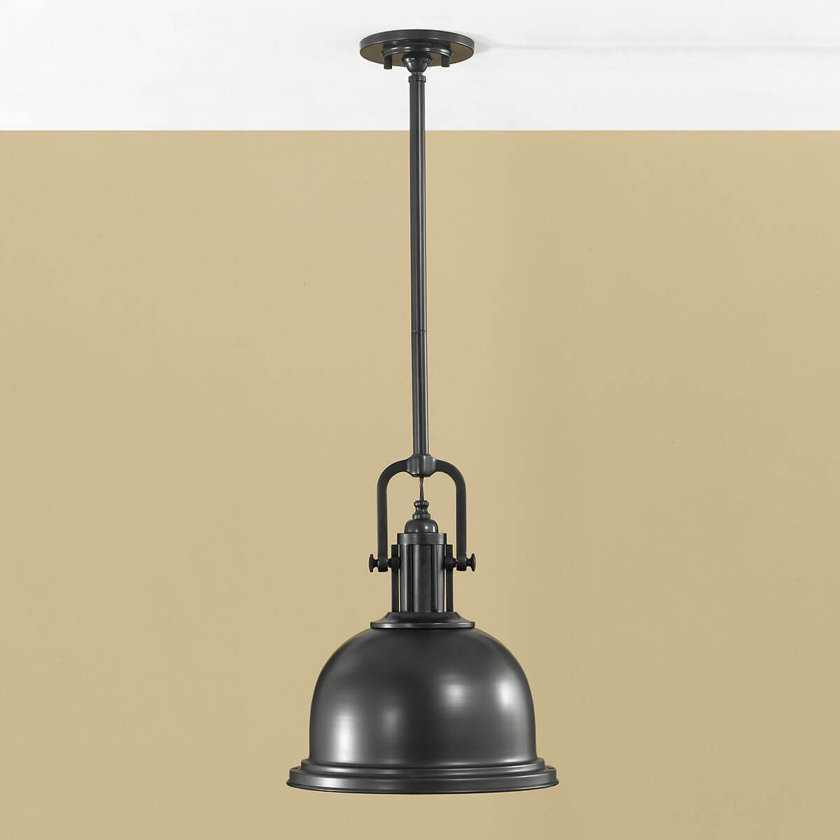Luminaire suspendu photographié en intérieur devant un mur beige, montrant sa fixation au plafond