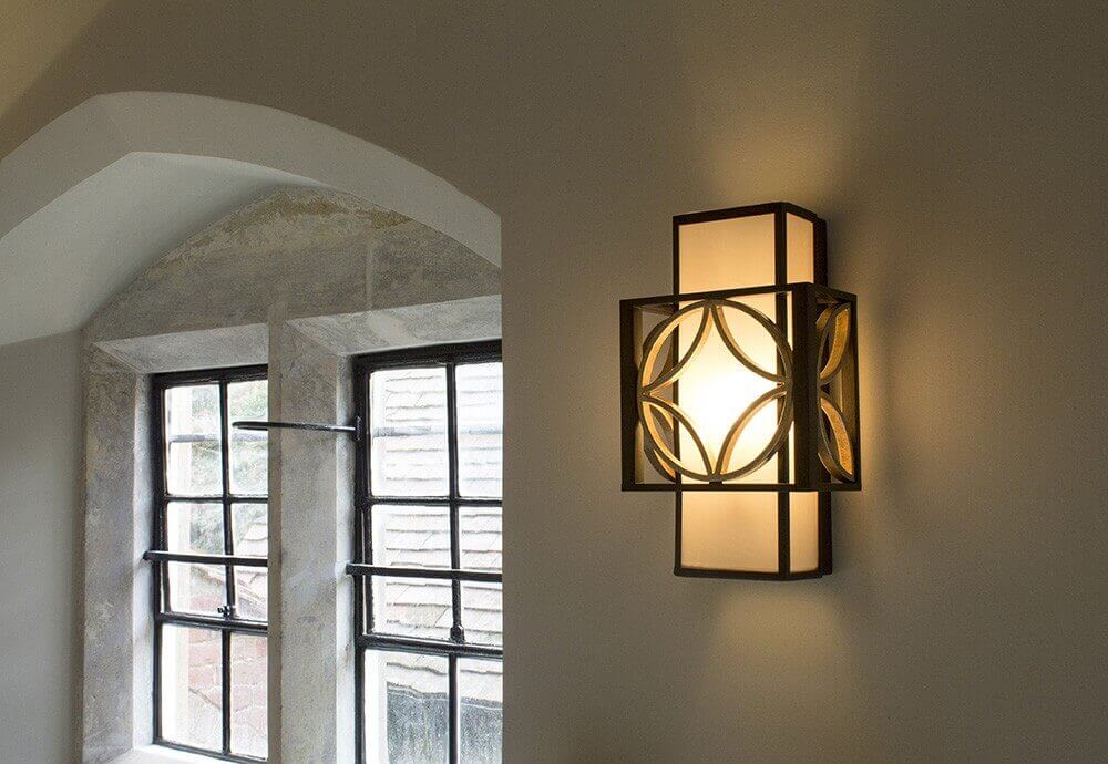 Applique murale allumée fixée sur un mur, près d'une fenêtre cintrée, diffusant une lumière chaude.