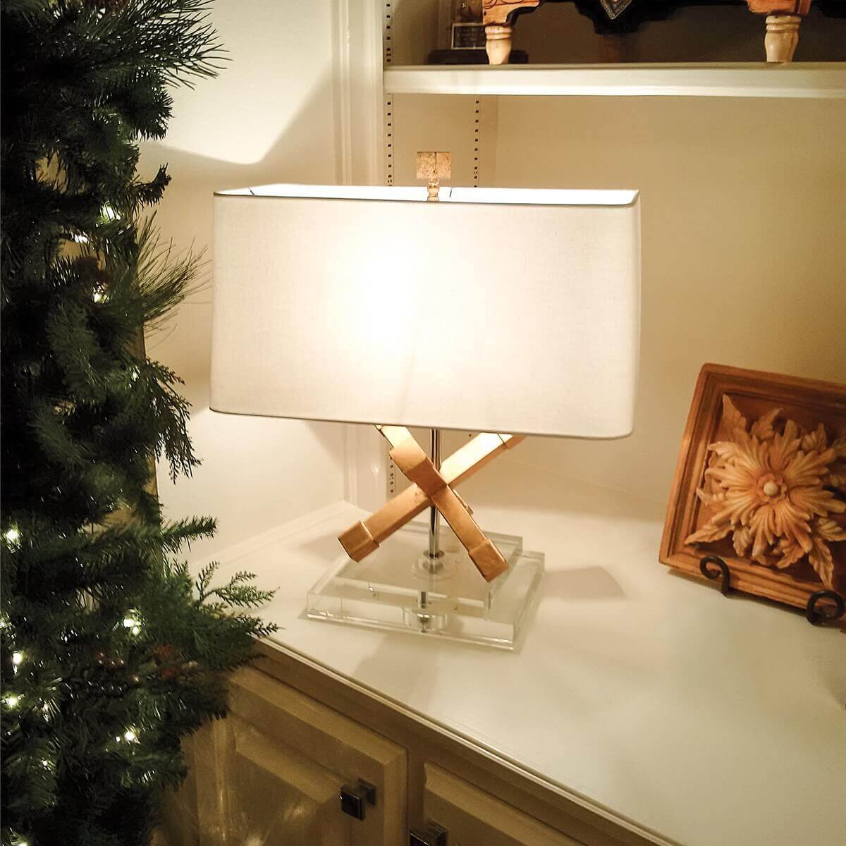 Mise en ambiance sur un meuble clair, lampe allumée près d'une branche de sapin
