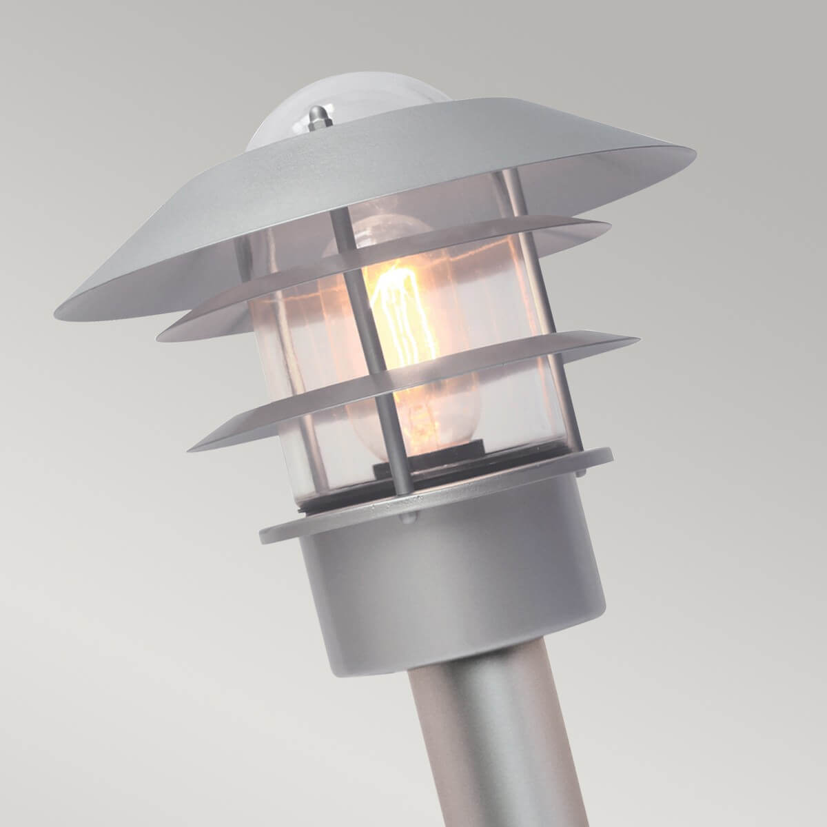 Gros plan sur la tête du luminaire, ampoule allumée sous capot et ailettes