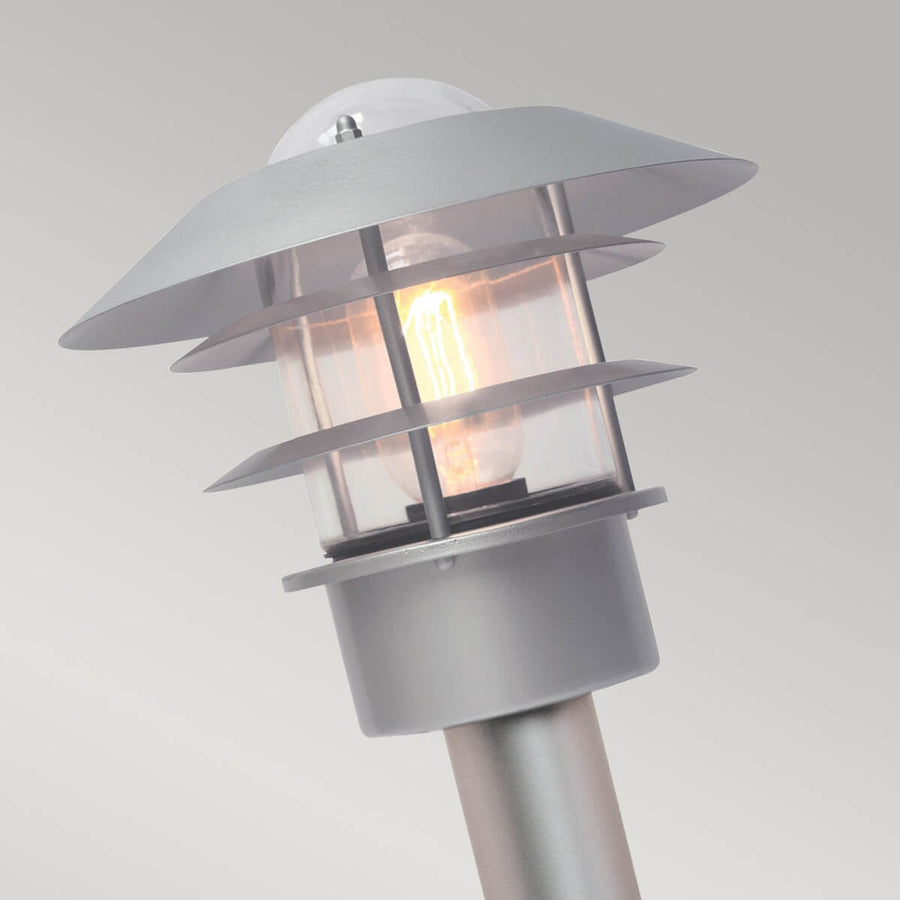 Gros plan sur la tête du luminaire, ampoule allumée sous capot et ailettes