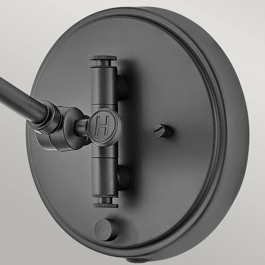 Détail de la platine murale ronde noire avec logo H et vis de fixation apparente.