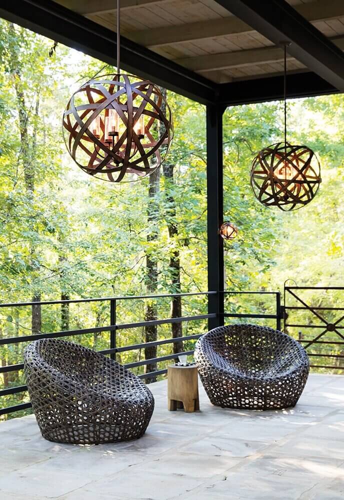 Mise en ambiance sur une terrasse couverte, deux suspensions au-dessus de fauteuils tressés