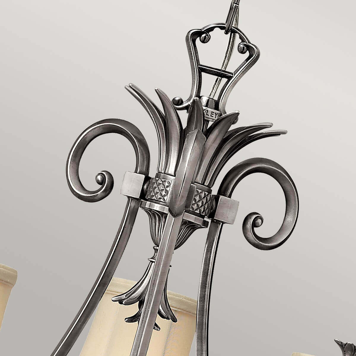 Détail du sommet ornementé avec volutes, feuilles métalliques et attache supérieure.