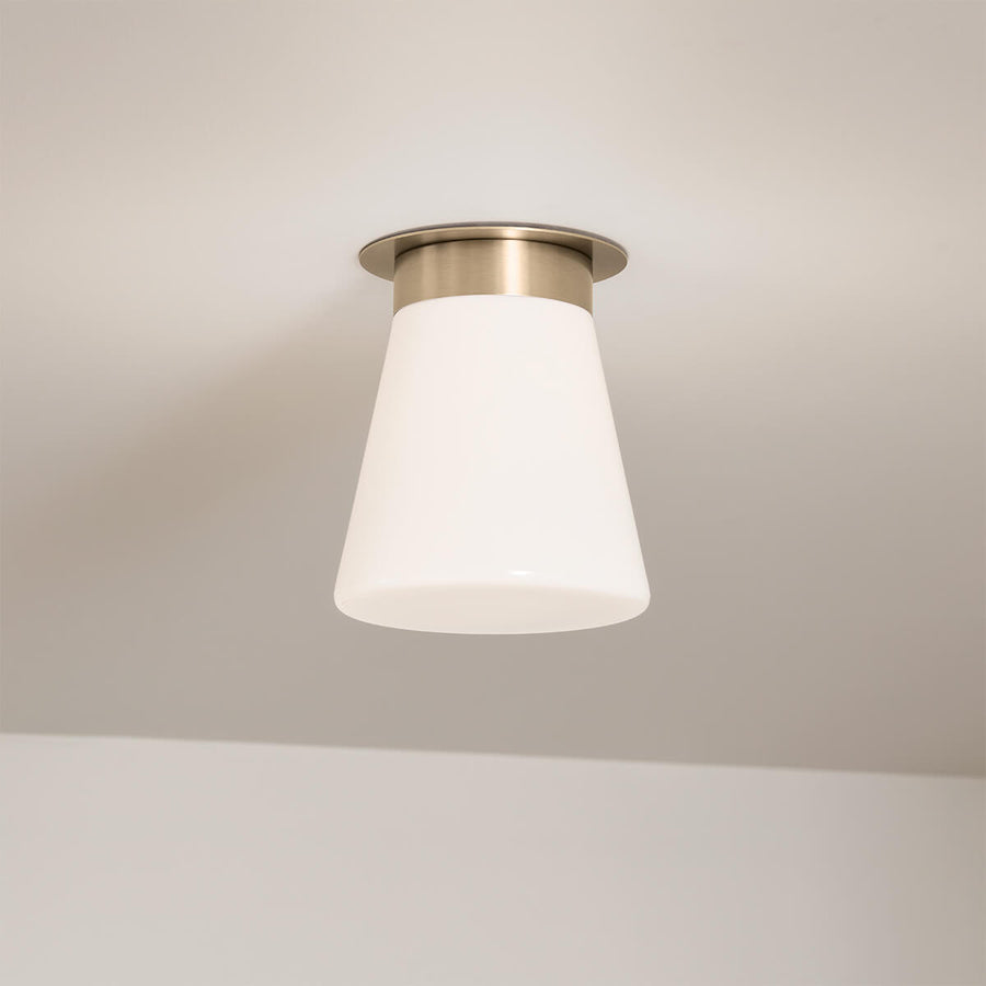 Luminaire installé au plafond, éclairé, montrant sa silhouette conique et ses proportions