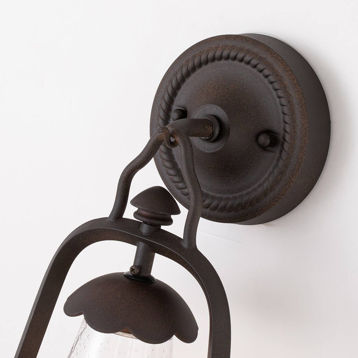 Détail de la platine murale ronde avec motif torsadé et bras recourbé en bronze.