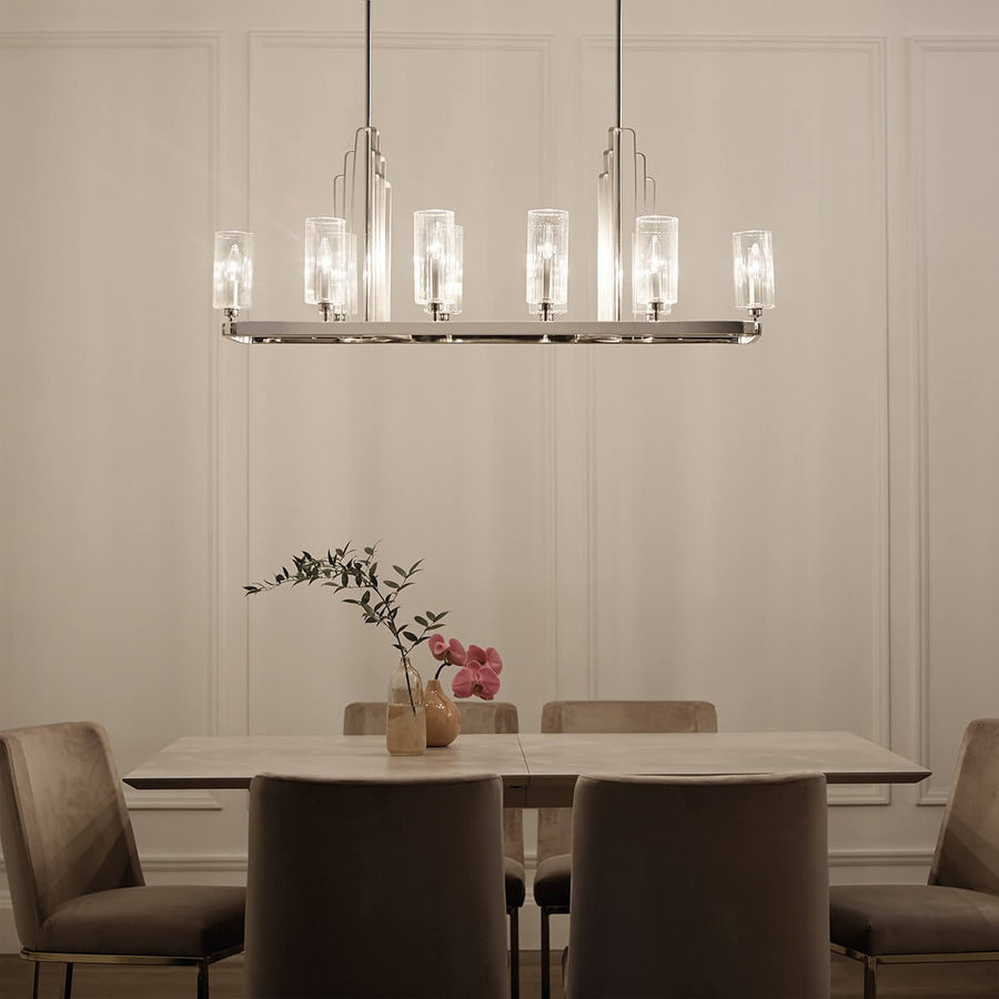 Lustre allumé éclairant une salle à manger blanche avec chaises en velours