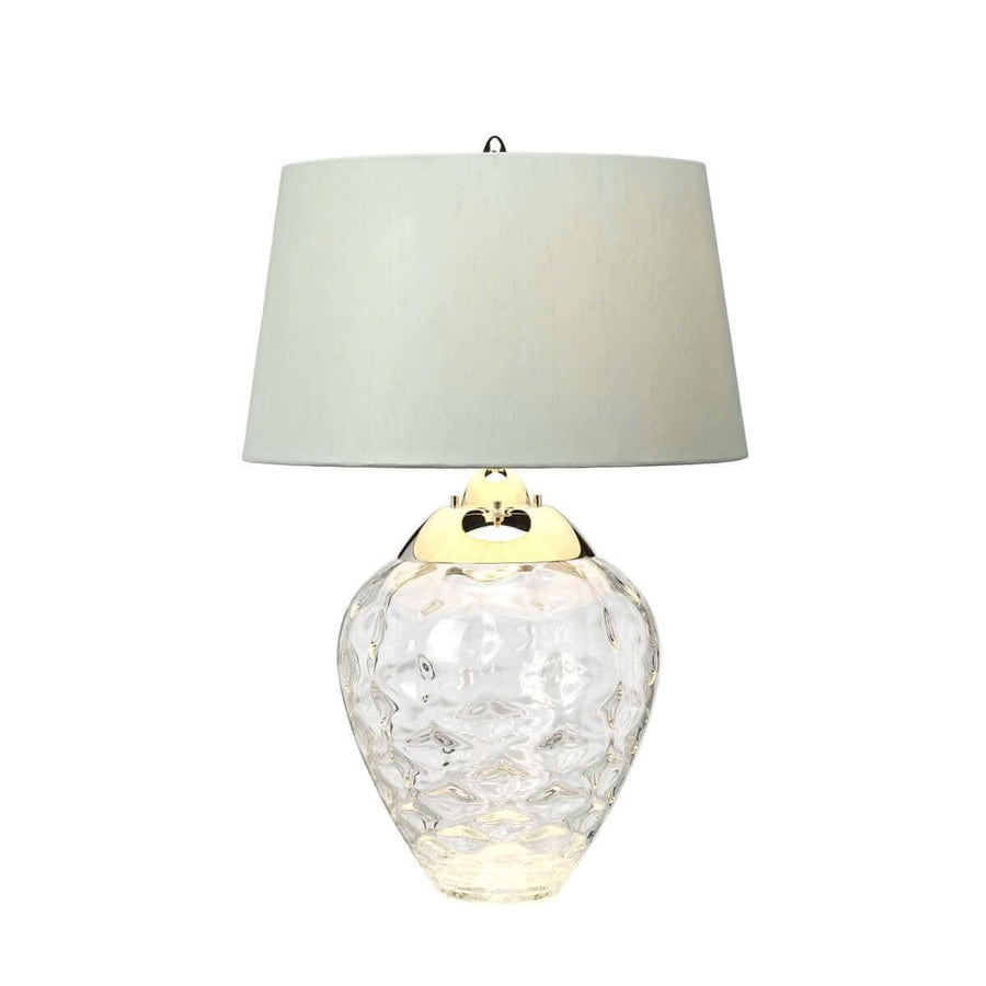 Lampe à poser avec détails dorés, verre transparent et lumière chaude.