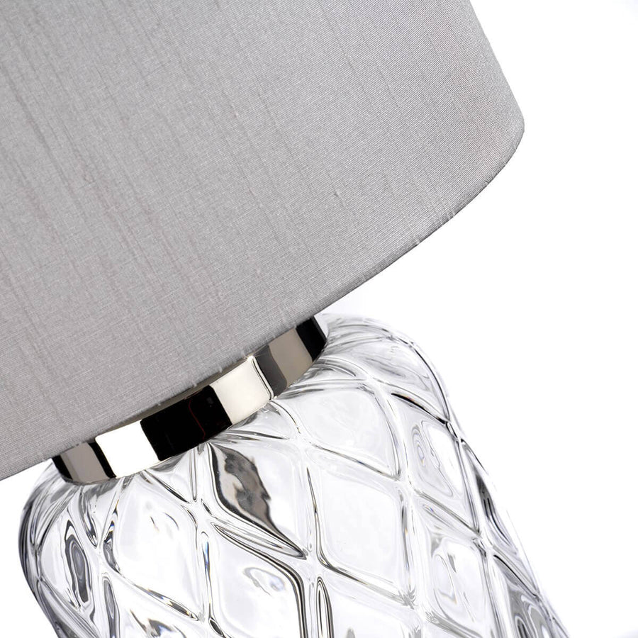 Détail du raccord en nickel poli entre l'abat-jour gris et la base en verre moulé.