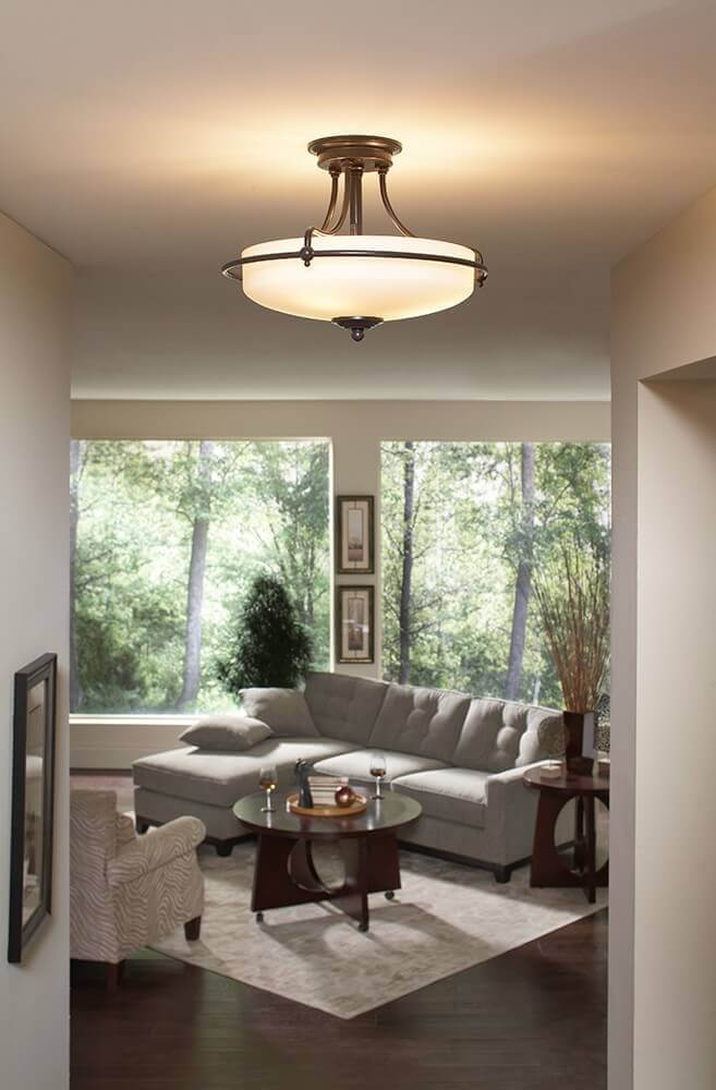 Luminaire allumé au plafond d'un salon moderne avec canapé, table et vue sur des arbres.