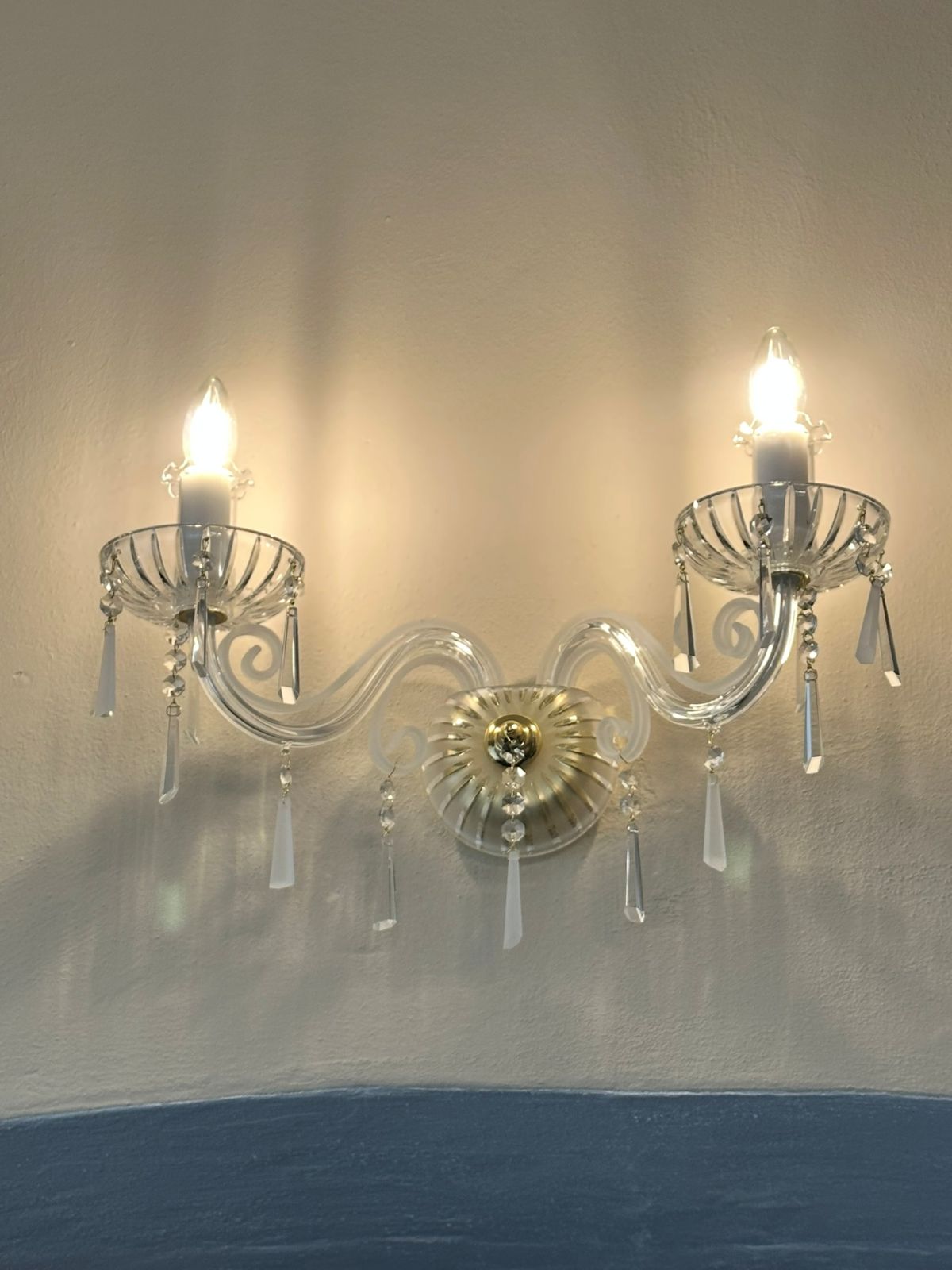 Vue en situation : applique allumée sur mur clair, lumière chaude et ombres portées.