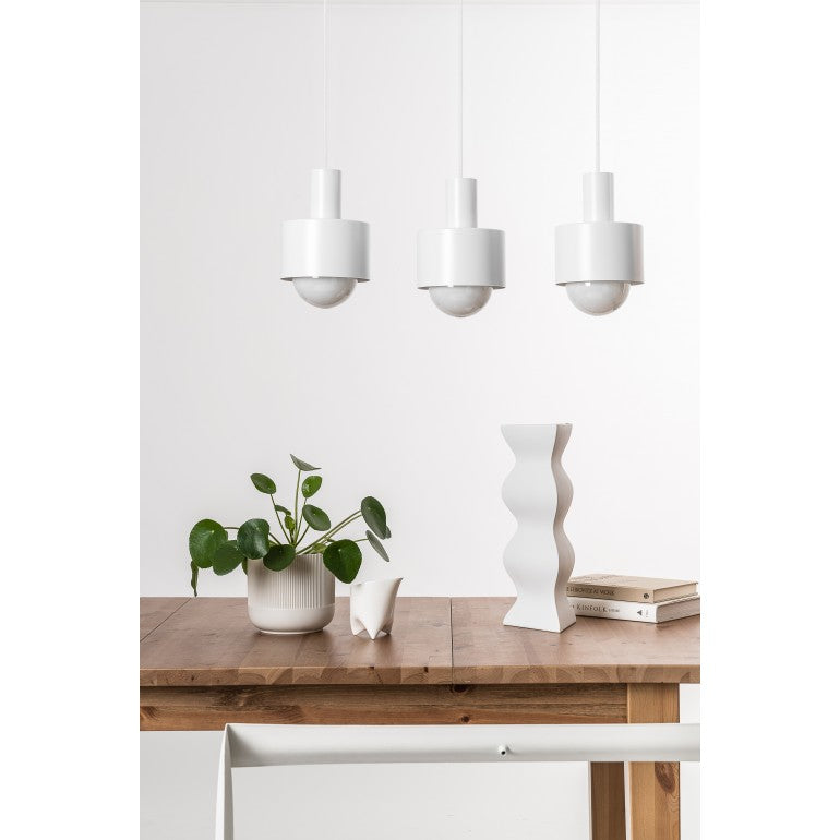 Mise en ambiance au-dessus d'une table en bois, suspension blanche et décor végétal.
