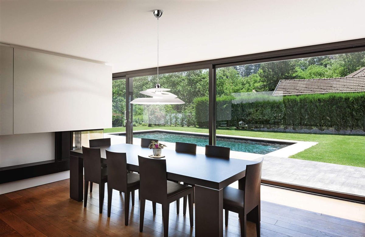 Mise en ambiance au-dessus d'une table sombre, baie vitrée ouvrant sur piscine et jardin verdoyant